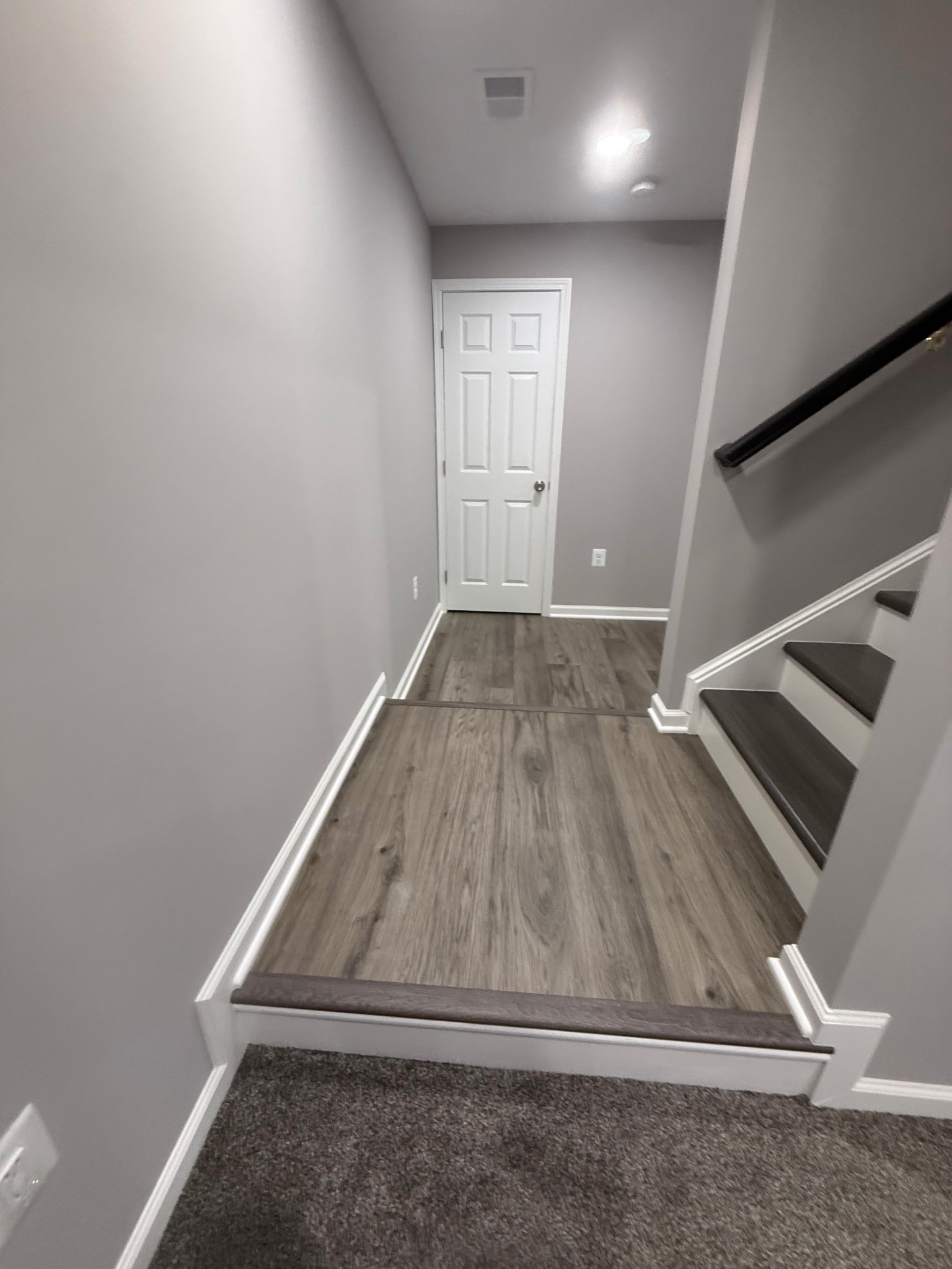 Finished basement hall and stair landing with plank flooring and painted walls