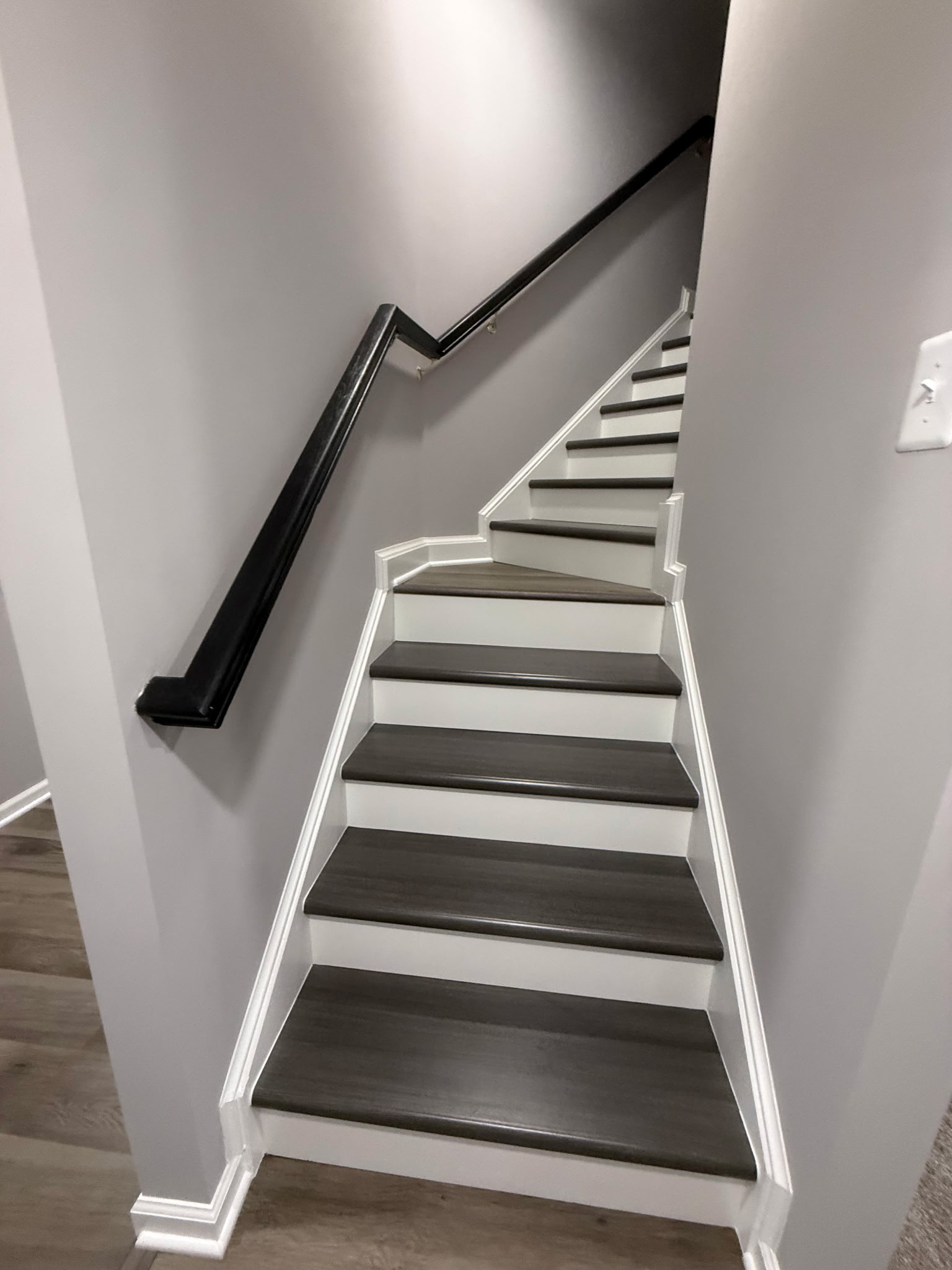 Finished basement staircase with dark treads, white risers, trim, and handrail