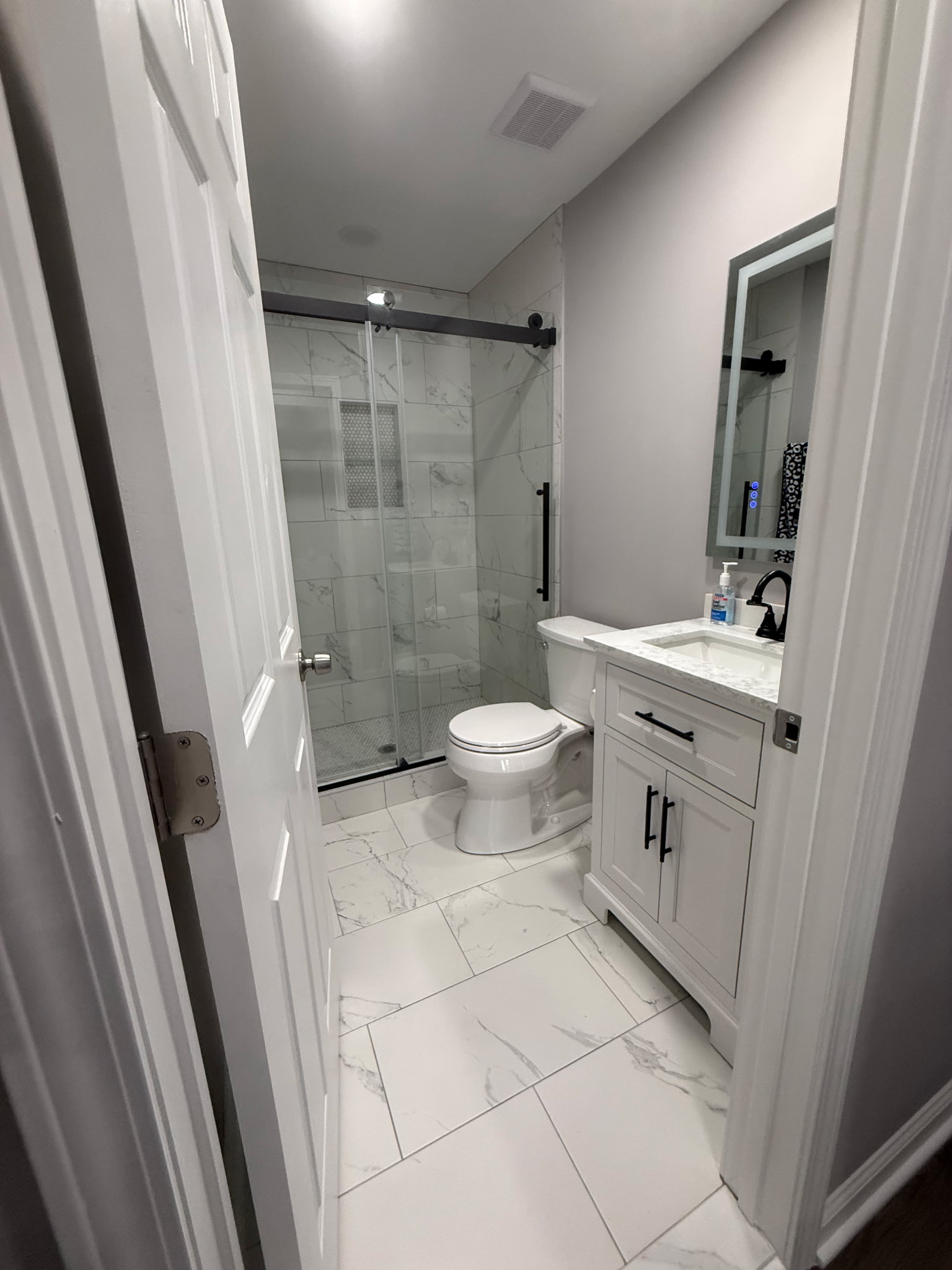 Finished basement bathroom with tiled shower, vanity, and coordinated black fixtures